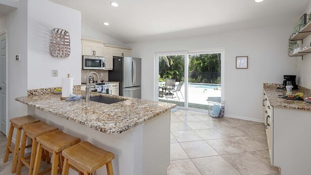 Una cocina moderna con encimeras de granito, electrodomésticos de acero inoxidable y vistas a una piscina en el patio trasero.