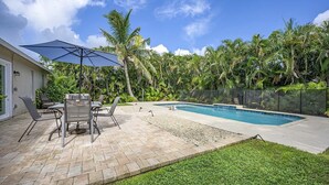 Un patio trasero con piscina, muebles de jardín y una zona de estar techada.