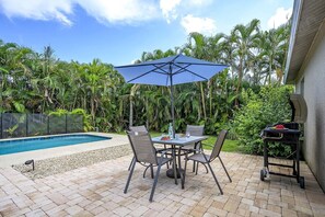 Une terrasse avec une piscine, entourée de palmiers et dotée d’un barbecue.