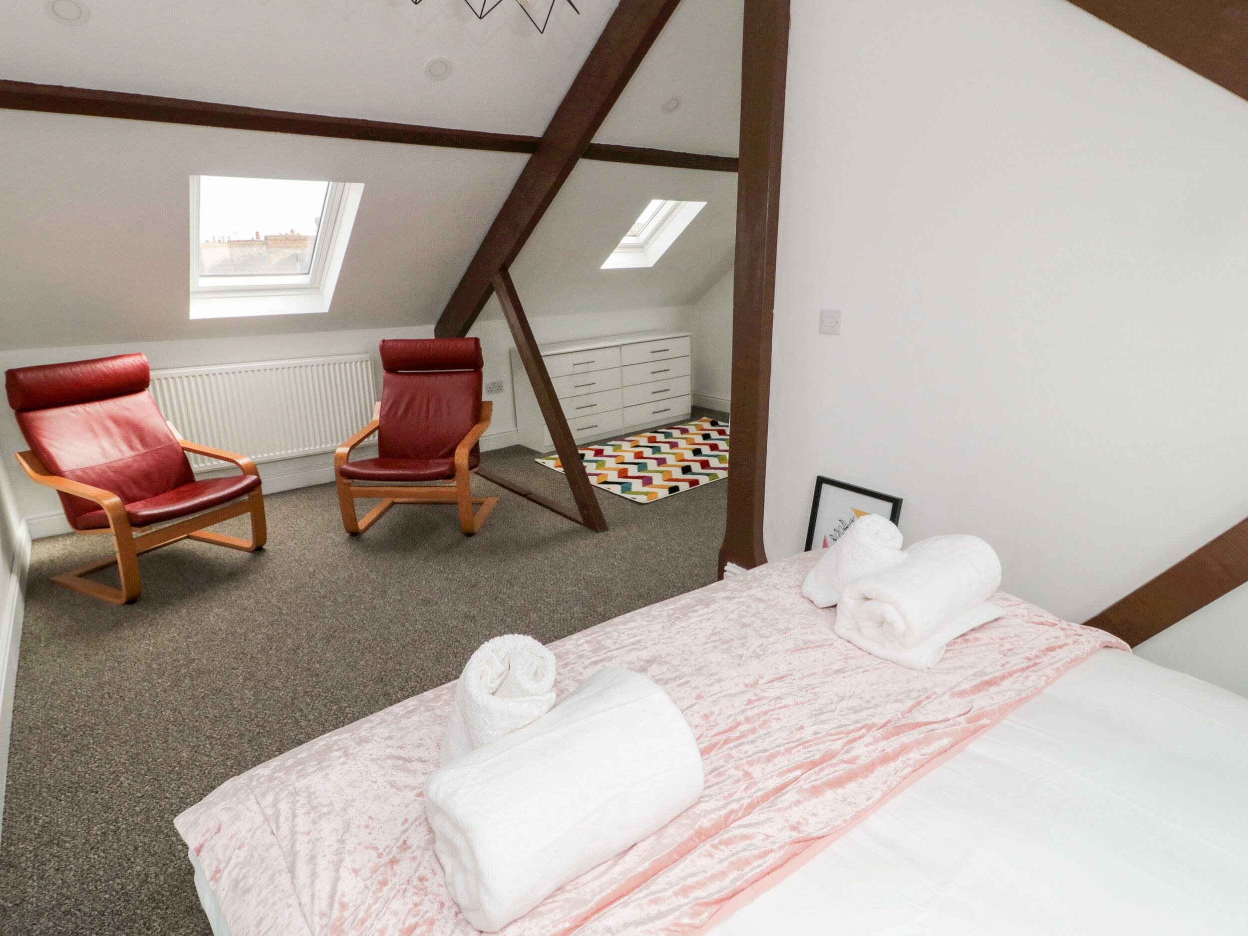 Ein Schlafzimmer mit einem Bett, zwei roten Stühlen, einer Holzleiter, einem Heizkörper und einem Fenster.