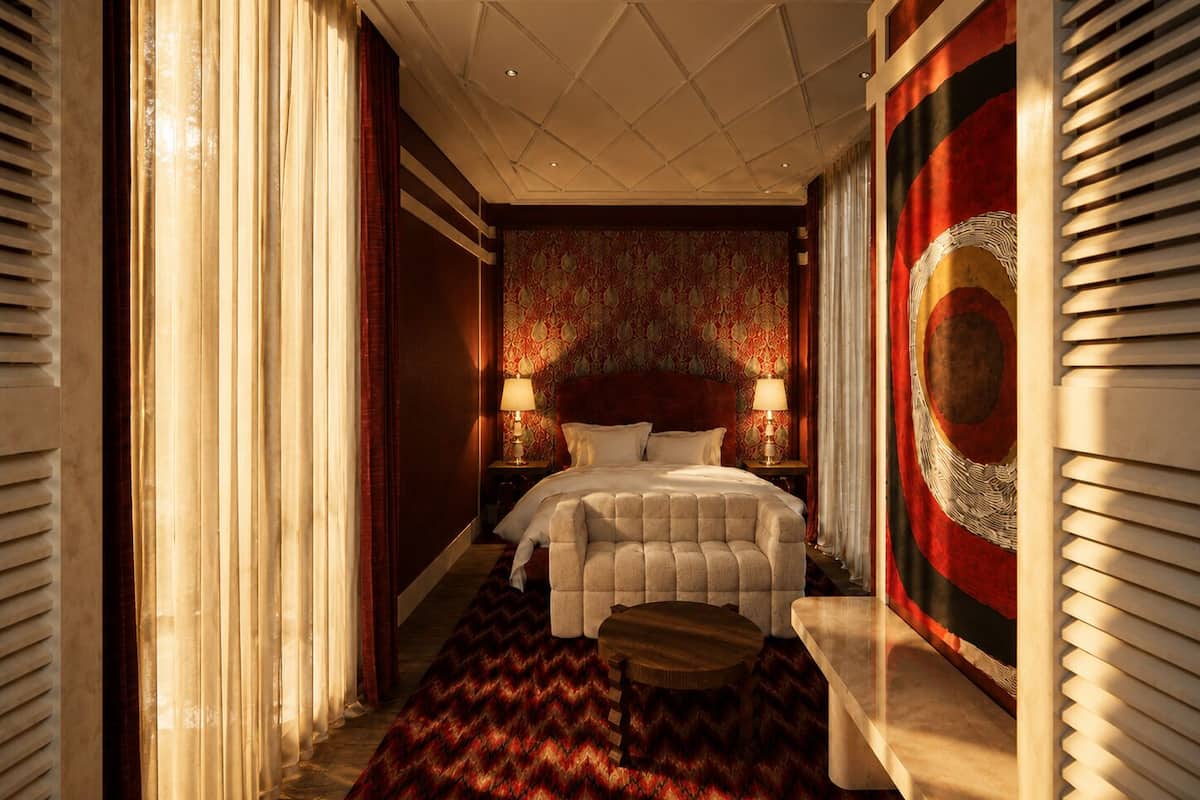 Une chambre d’hôtel avec un grand lit, deux tables de chevet avec des lampes, une moquette à motifs et une grande tapisserie au mur.