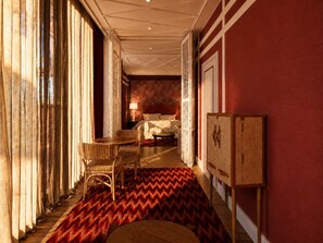 A hotel room with a bed, a sitting area with a table and chairs, a large window with curtains, and a patterned rug. - Hotel Club 29 (Barcelona)