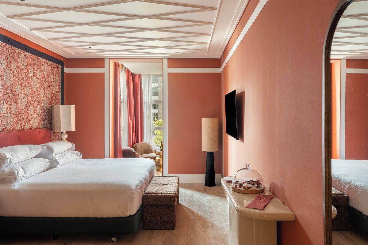 A hotel room with a large bed, a desk with a lamp, a television, and a view of the outdoors.