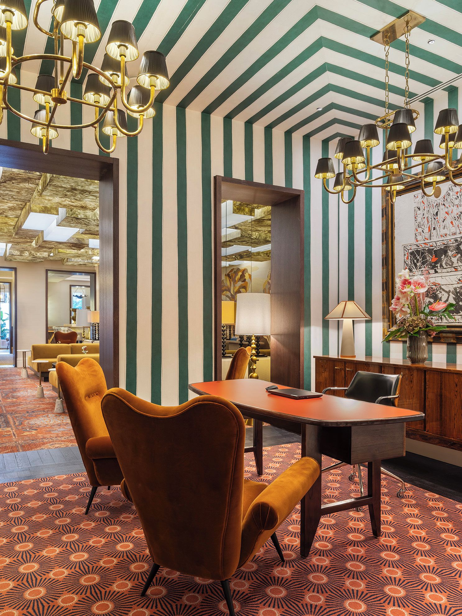 A hotel room with striped walls, a chandelier, a dining table with chairs, and a patterned carpet.