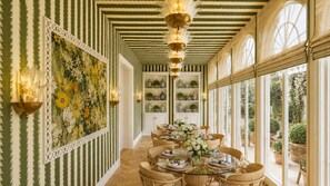 Un espace repas comprenant une longue table, des chaises et un mur décoratif orné d’un tableau représentant des motifs floraux.