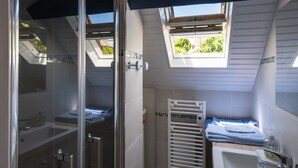 Une salle de bain moderne avec une douche à l’italienne en verre, une baignoire blanche et un puits de lumière.