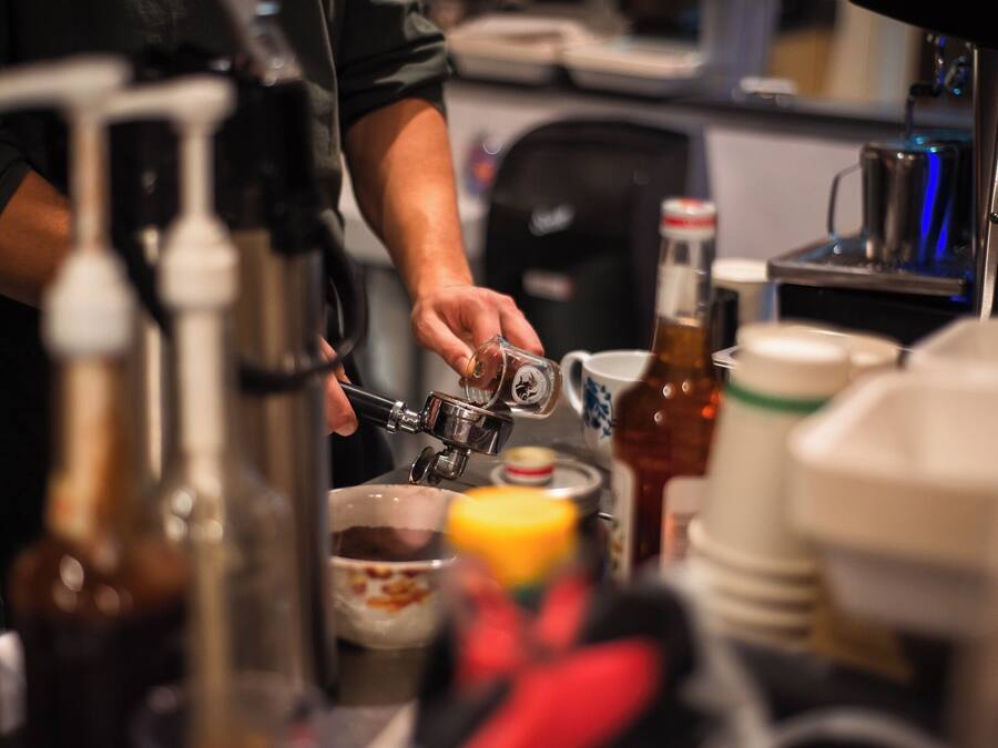 A person preparing a drink with a coffee machine, a bottle, and a mug on a counter.