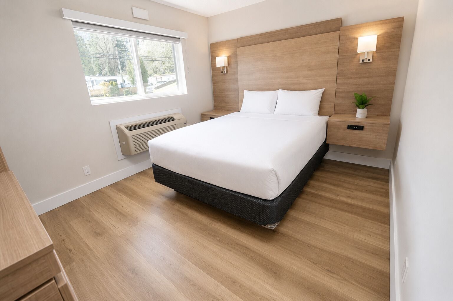A modern bedroom with a large bed, a window with blinds, a wall-mounted heater, and a bedside table with a plant.