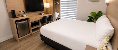 Een hotelkamer met een bed, een televisie, een bureau met een koffiezetapparaat, een minibar en een potplant.