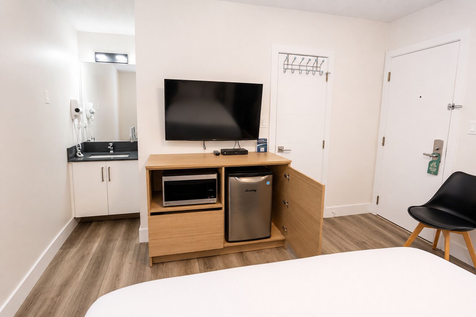 Una camera d'albergo con un letto, una televisione, un forno a microonde, un frigorifero, un lavandino e uno specchio.