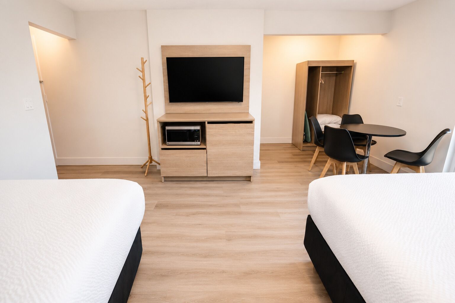 A hotel room with two beds, a TV, a microwave, a dining table with chairs, and a coat rack.