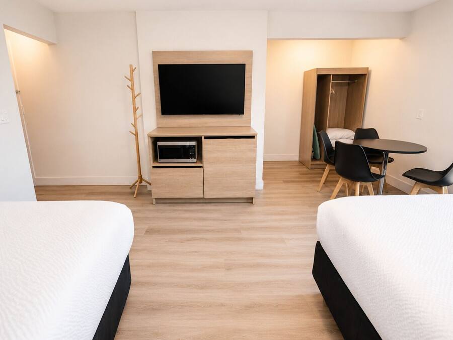 Habitación de hotel con dos camas, un televisor, un microondas, una mesa de comedor con sillas y un perchero.