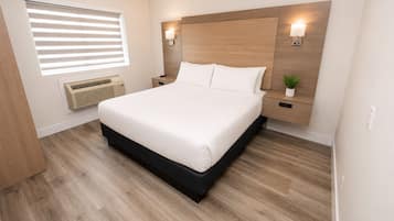 A neatly arranged bedroom with a bed, bedside tables, wall-mounted lights, and a window with blinds.