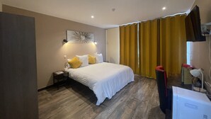A hotel room with a bed, a nightstand, a TV, and a desk with a computer. - Leclerc hôtel (Le Mans)