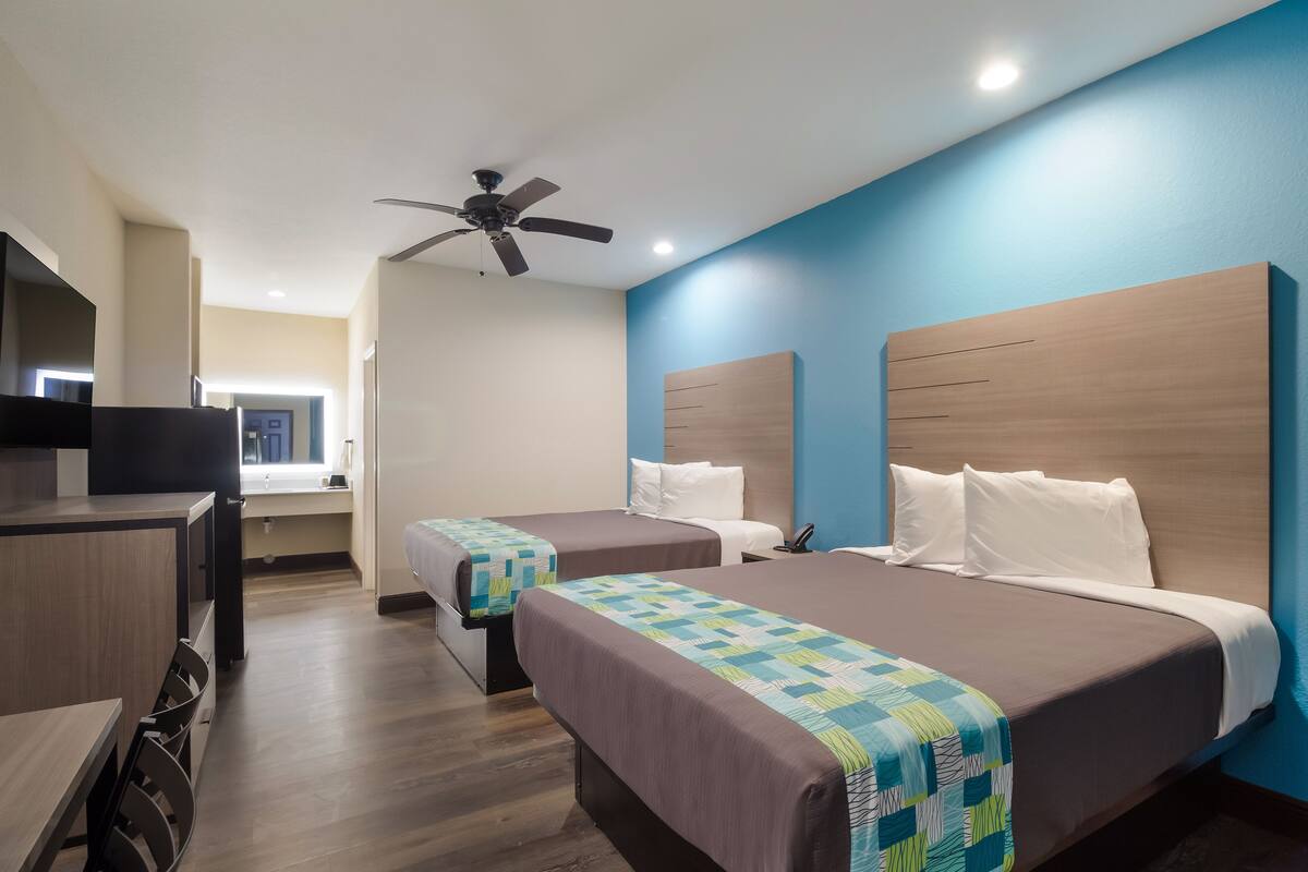 A hotel room with two beds, a desk, a ceiling fan, and a TV.