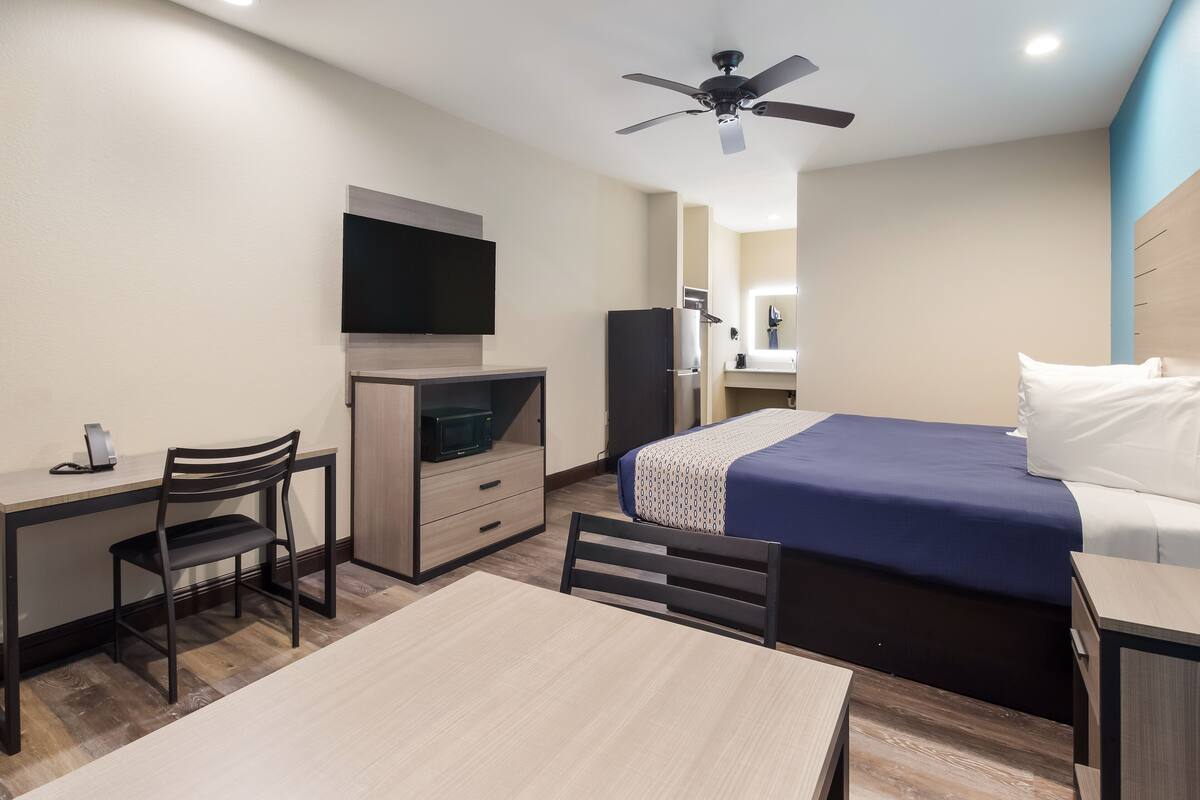 A hotel room with a bed, desk, chair, television, wardrobe, and ceiling fan.