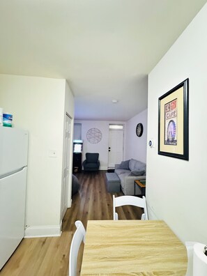 Un espacio habitable compacto con comedor, kitchenette, sofá gris y un reloj en la pared.