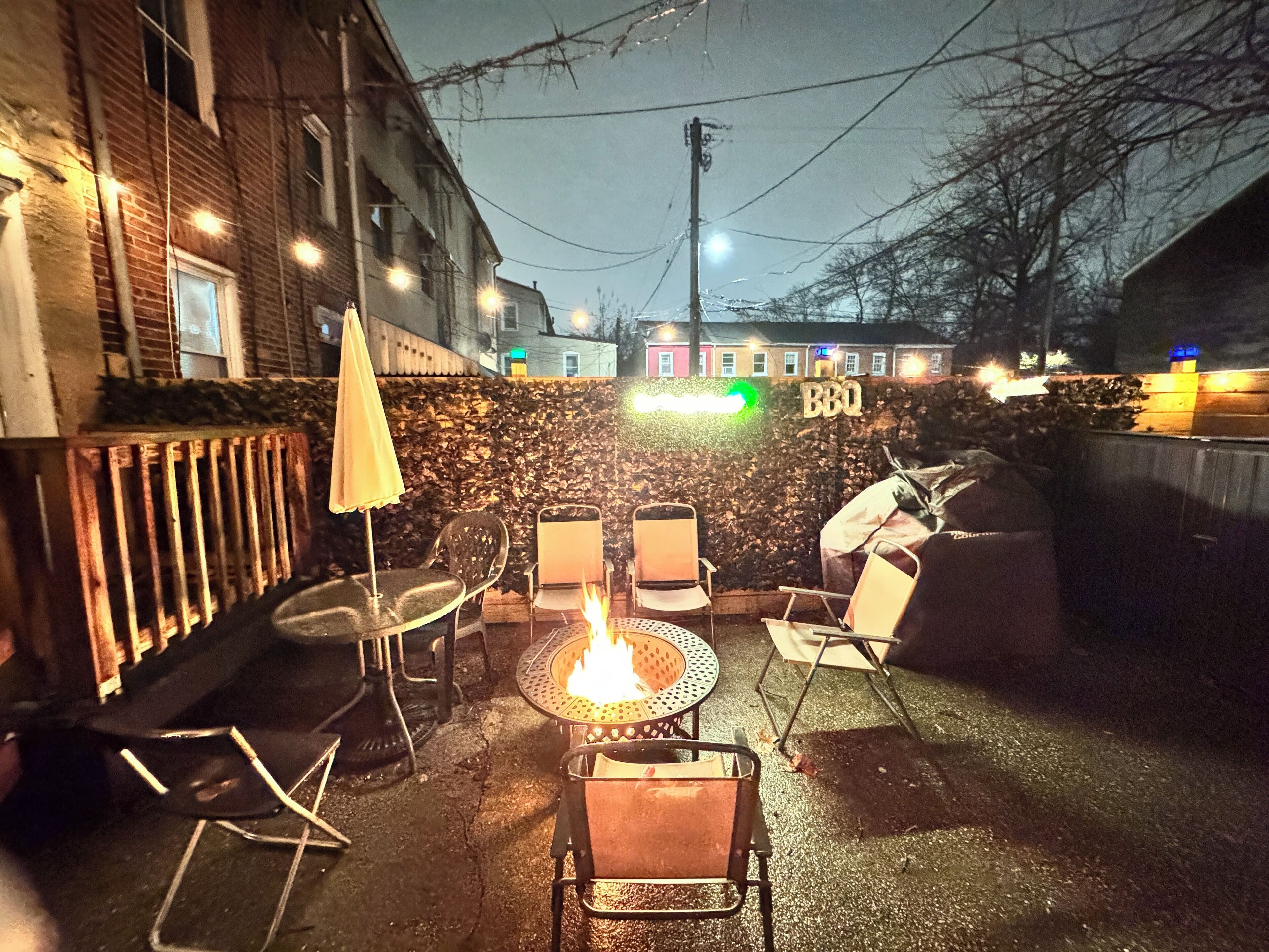 An outdoor patio with metal chairs and a table, a small fire, and a sign that reads "BBQ".