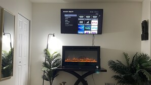 Un salón con televisión de pantalla plana en la pared, una chimenea y dos plantas en macetas.