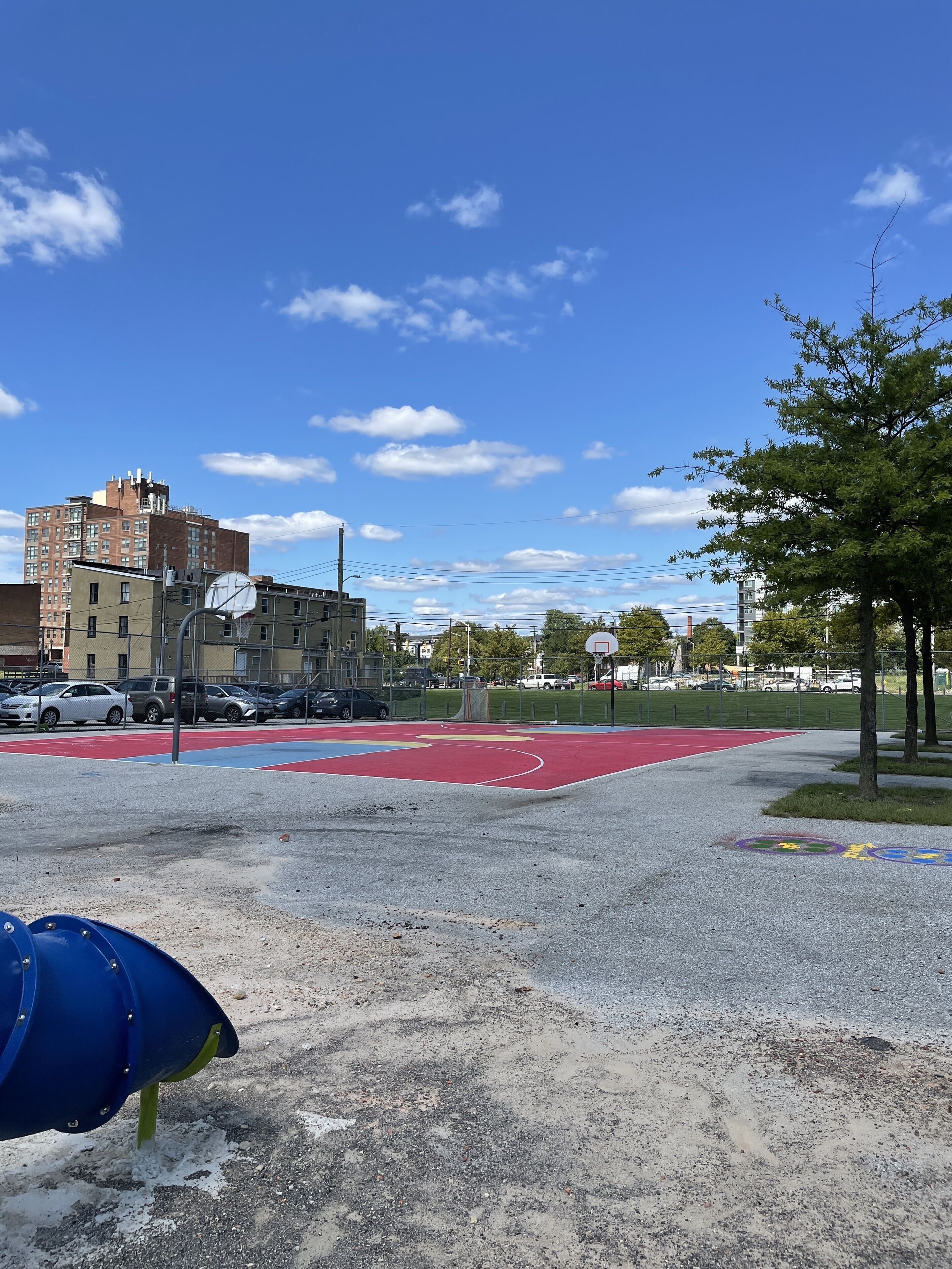 A playground with a basketball court, a blue play structure, and a red running track.