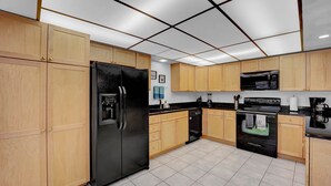 Een moderne keuken met houten kastjes, een zwarte koelkast, een magnetron, een oven en een vaatwasser.