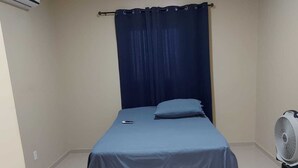 A small, neatly arranged bedroom with a single bed, a ceiling fan, and an air conditioning unit.