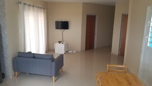 A living room with a sofa, a TV on a stand, a wooden table, and a door in the background.