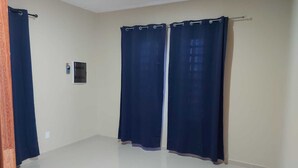 A room with a tiled floor, two dark curtains, and a small wall-mounted thermostat.