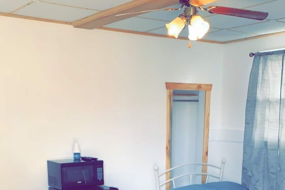 Quarto com duas camas, ventilador de teto, aquecedor, espelho e janela com cortinas.