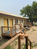Un motel con puertas numeradas, terrazas de madera al aire libre y mesas de picnic.