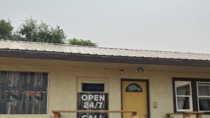 A small building with a yellow door, a sign indicating it's open 24/7, and a bench in front. - High Plains Inn (Newell)