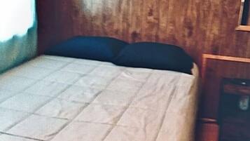 A bed with a quilted cover and two dark pillows in a room with wooden walls and a small window.