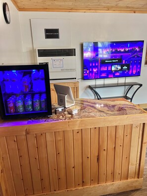 A reception desk with a mounted television displaying a cityscape, a clock on the wall, and a sign indicating check-out time.