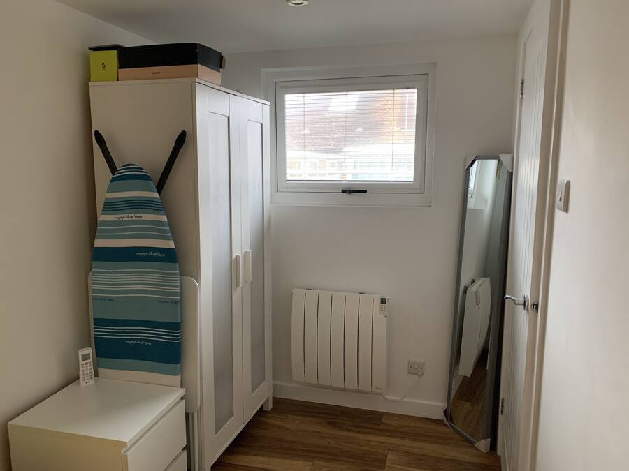 Un couloir étroit avec un radiateur blanc, une fenêtre avec des stores et un meuble blanc sur lequel sont posées des boîtes.