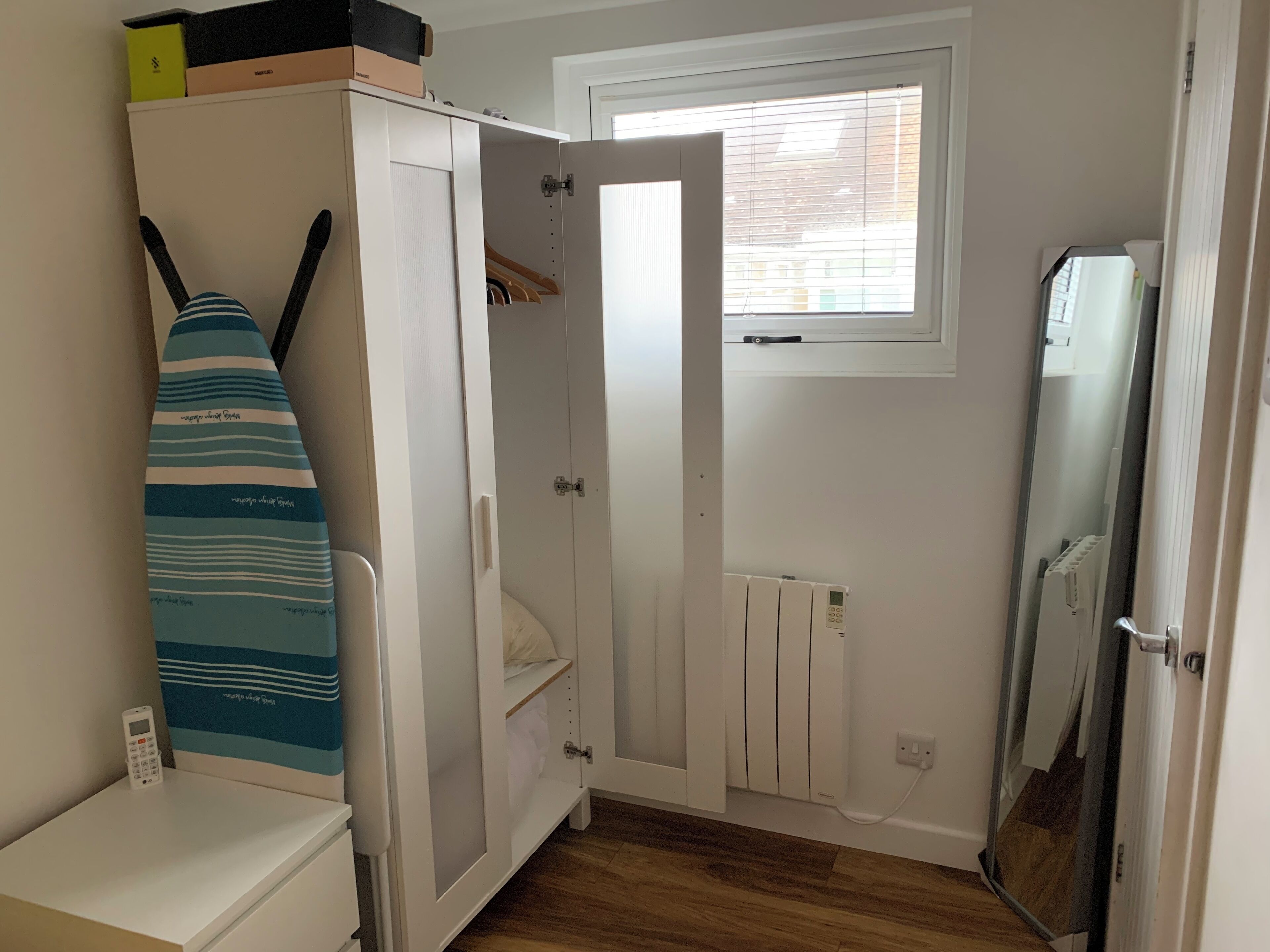 A compact room with a wardrobe, a small window, a radiator, and a mirror.