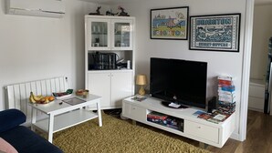 A living room with a white TV stand, a flat-screen TV, a white cabinet with glass doors, and two framed pictures on the wall. - Lodge , air con , Free Parking , Mini bar (Hove)