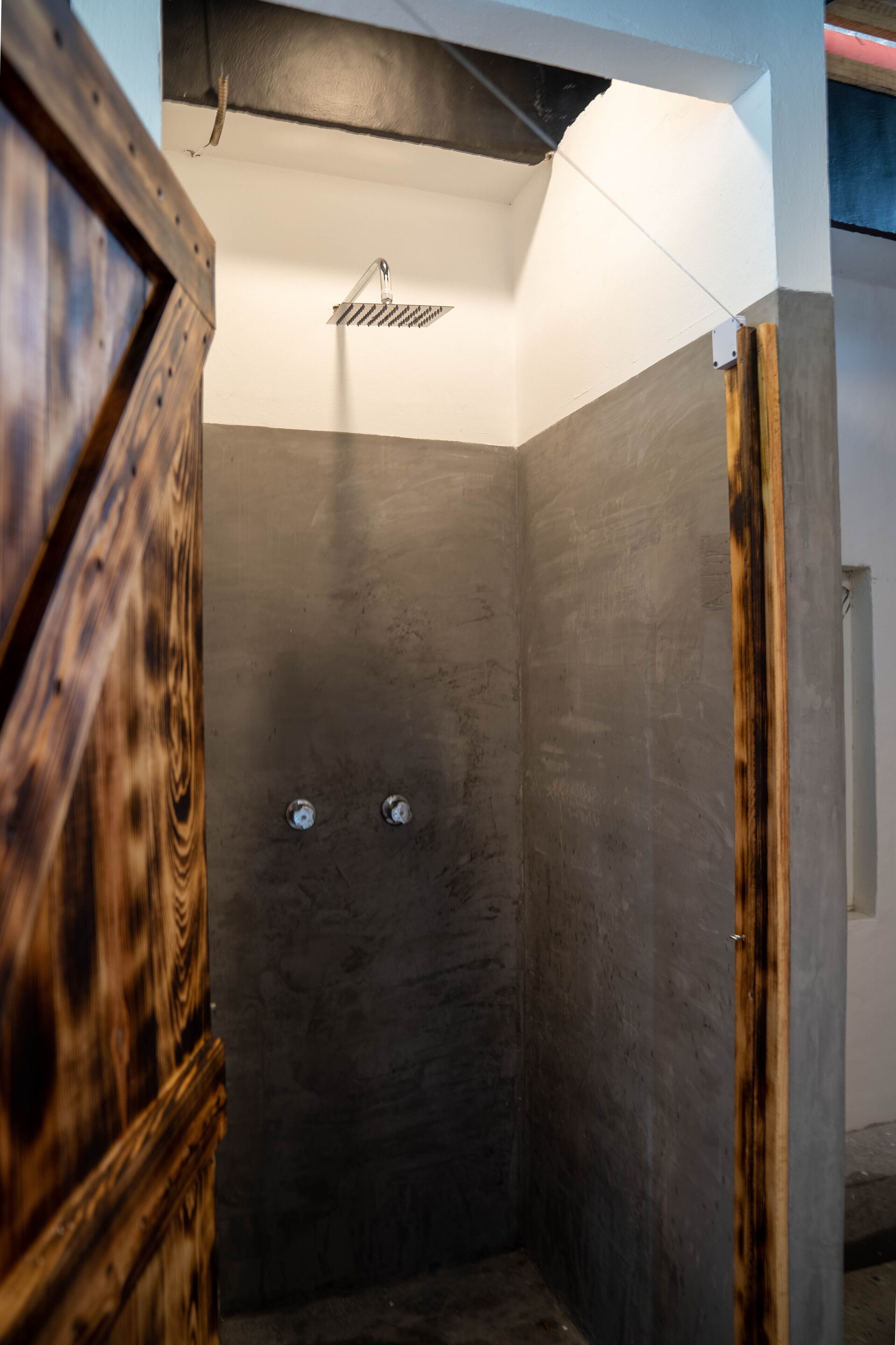 A shower with a wooden door and a metal showerhead.