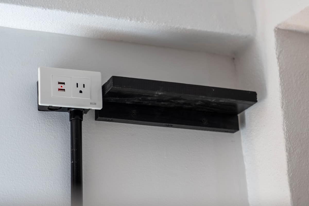 A white wall with a black electrical outlet and a black cable running along it.