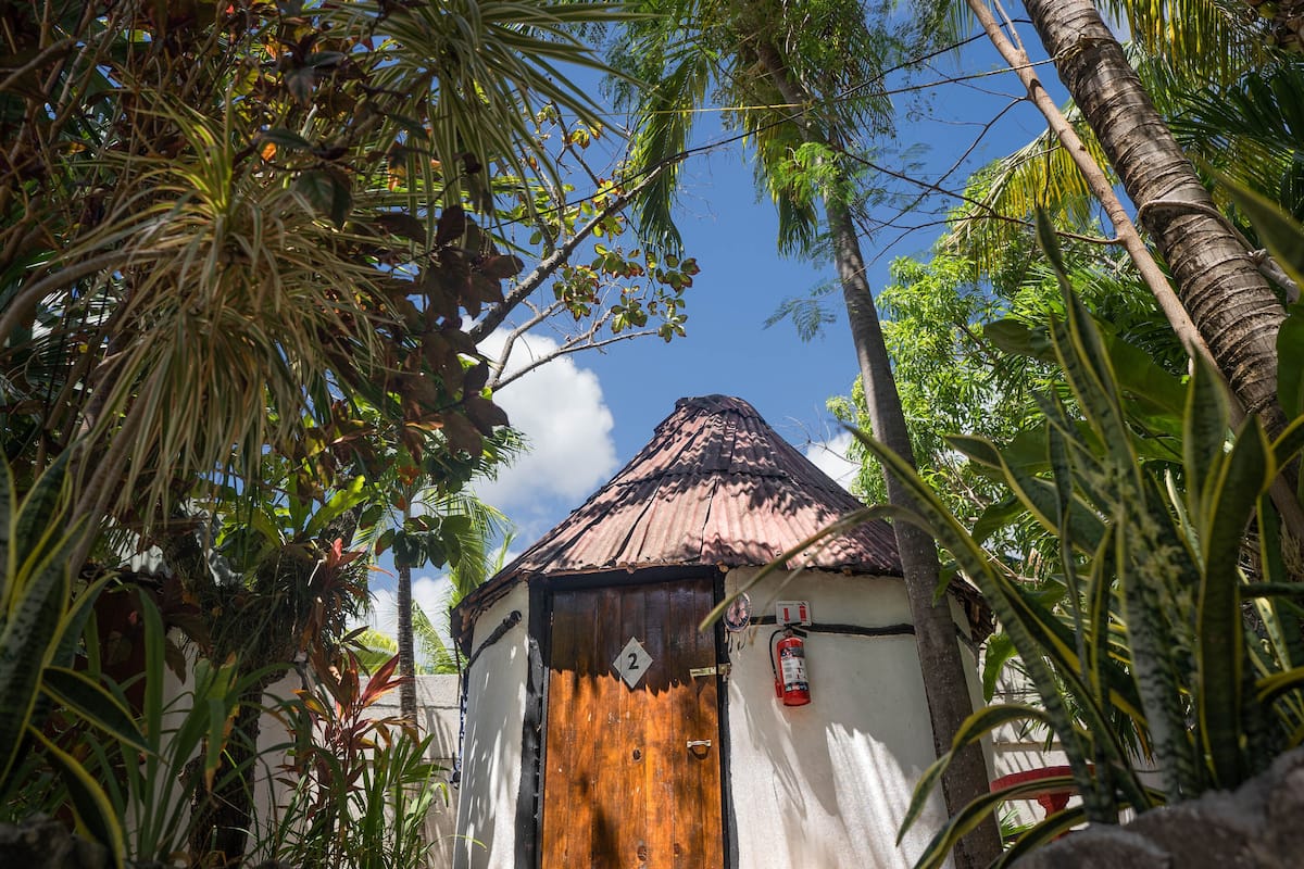 A small, rustic building with a thatched roof, surrounded by lush tropical vegetation.