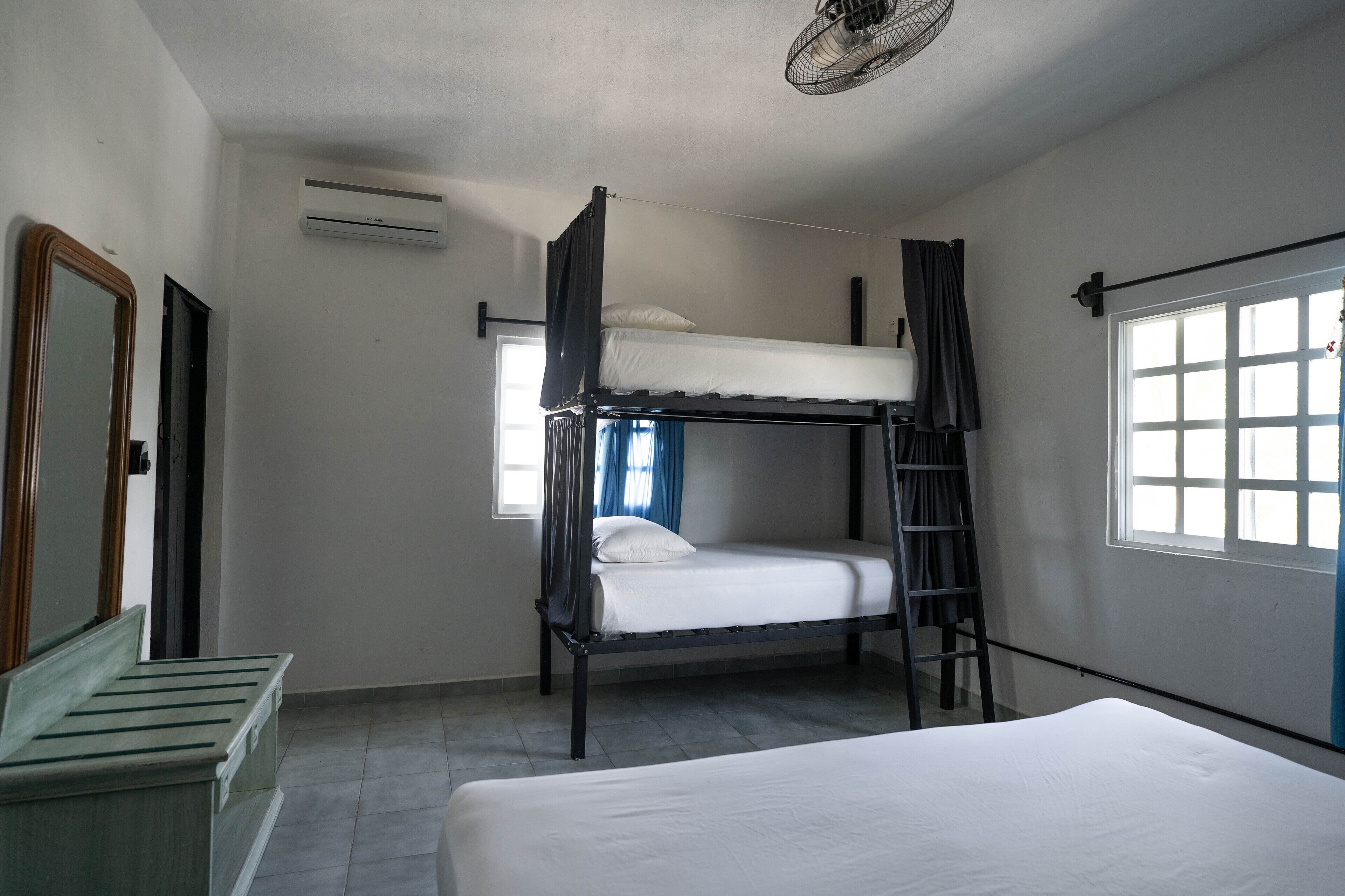 A bunk bed room with a ladder, a window with curtains, and a door.