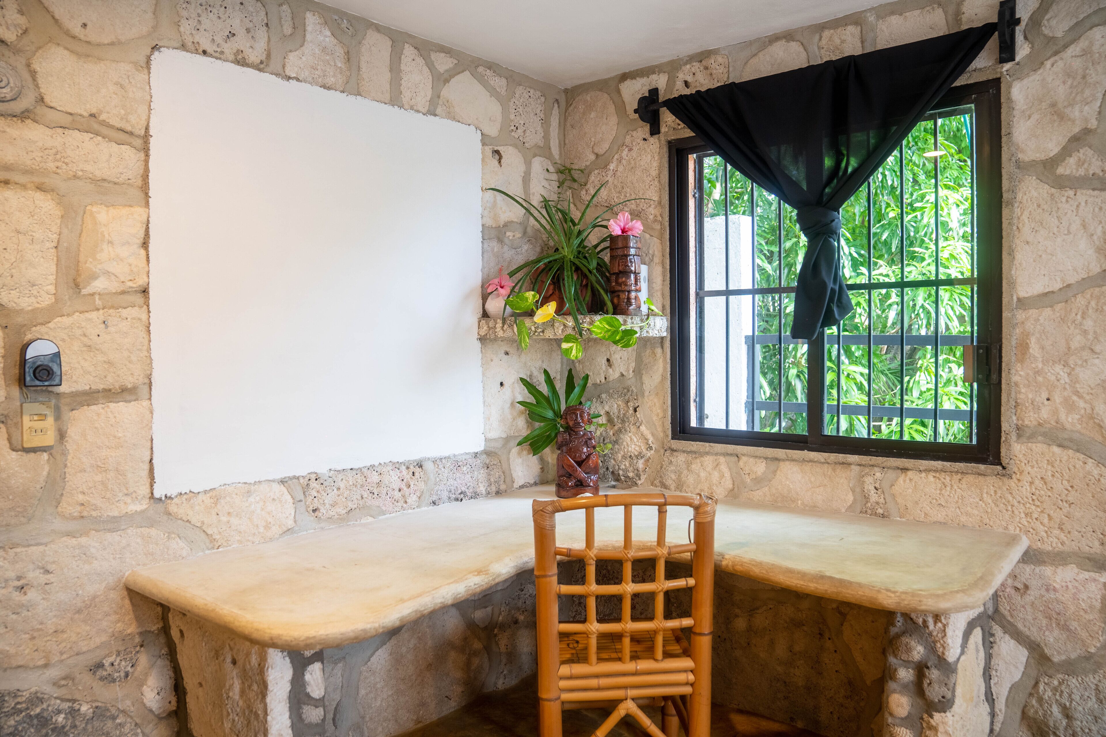 A stone-walled room with a wooden desk and chair, a window with a black curtain, and a whiteboard.