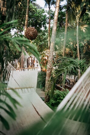 A hammock suspended between trees in a lush garden with a white fence and a wooden bench.