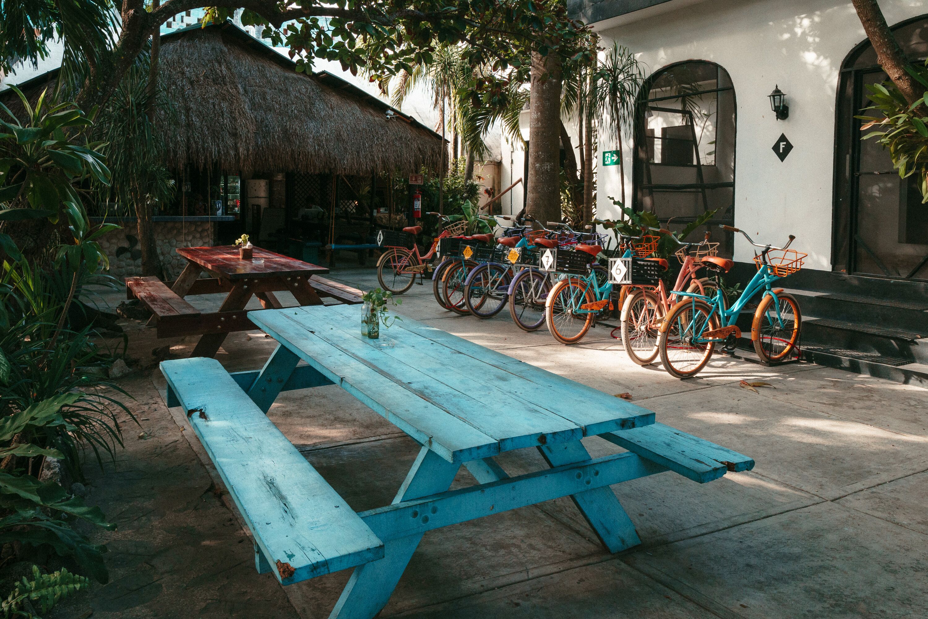 A patio area with a blue picnic table, several bicycles, and a thatched-roof structure.