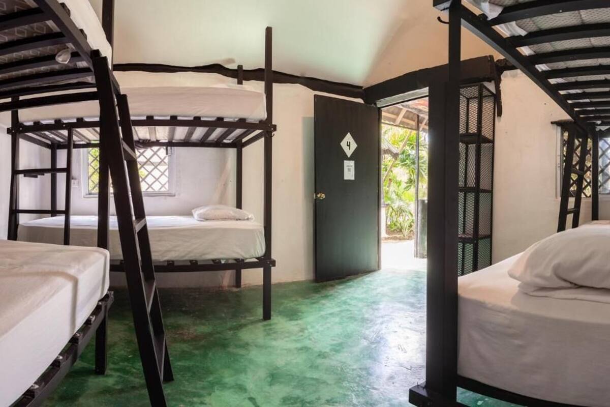 A room with bunk beds, a green floor, and a door with a number sign.