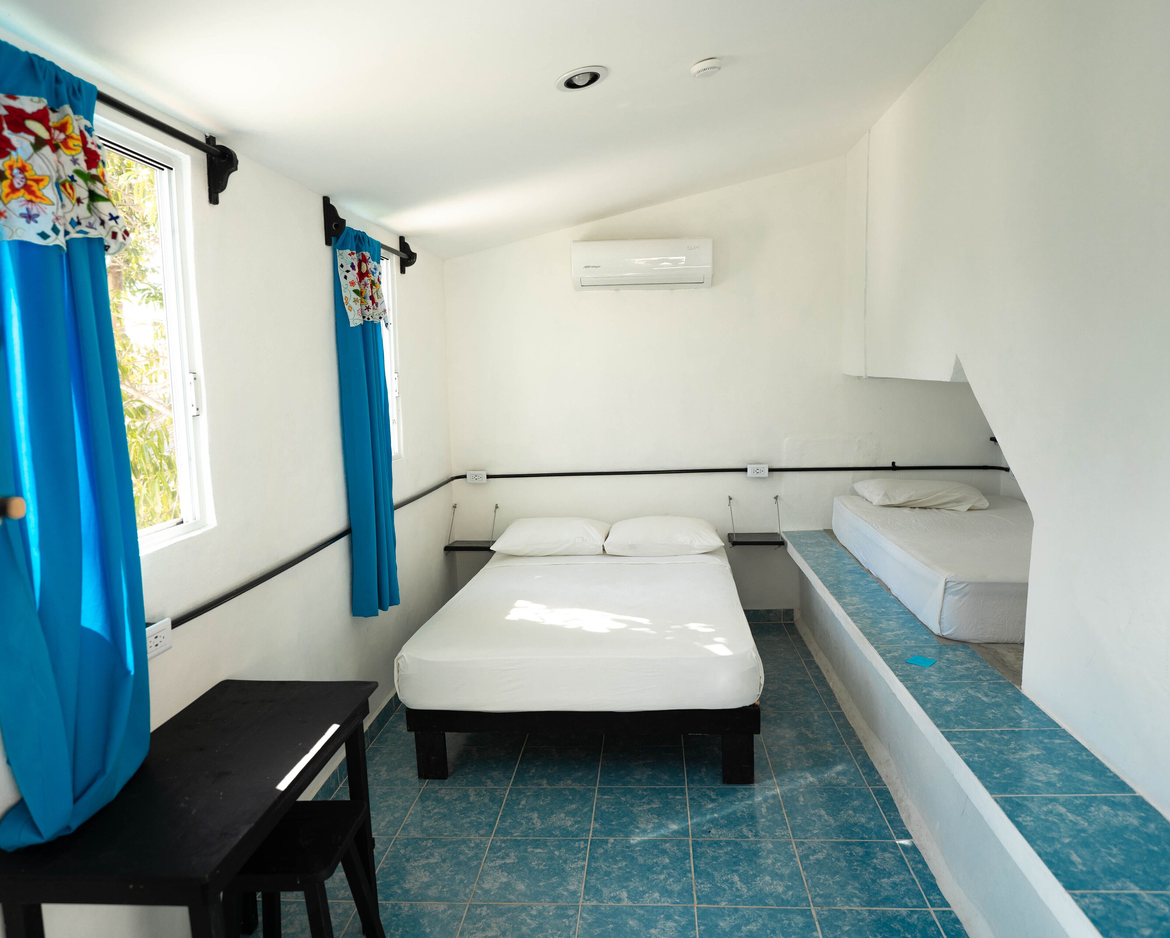 A small, clean room with a single bed, a desk, and a window with curtains.
