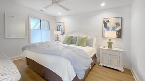 Une chambre à coucher avec un grand lit, deux tables de chevet avec des lampes, un ventilateur de plafond et des œuvres d’art accrochées aux murs.