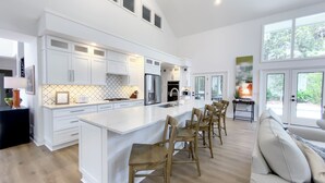 A modern kitchen with white cabinetry, a central island, and a dining area with wooden chairs. - 9 Sandhill Crane at Sea Pines Resort (Hilton Head Island)