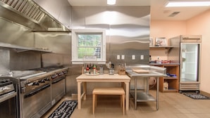 A kitchen with stainless steel appliances, a wooden table, and a window with a view of greenery.