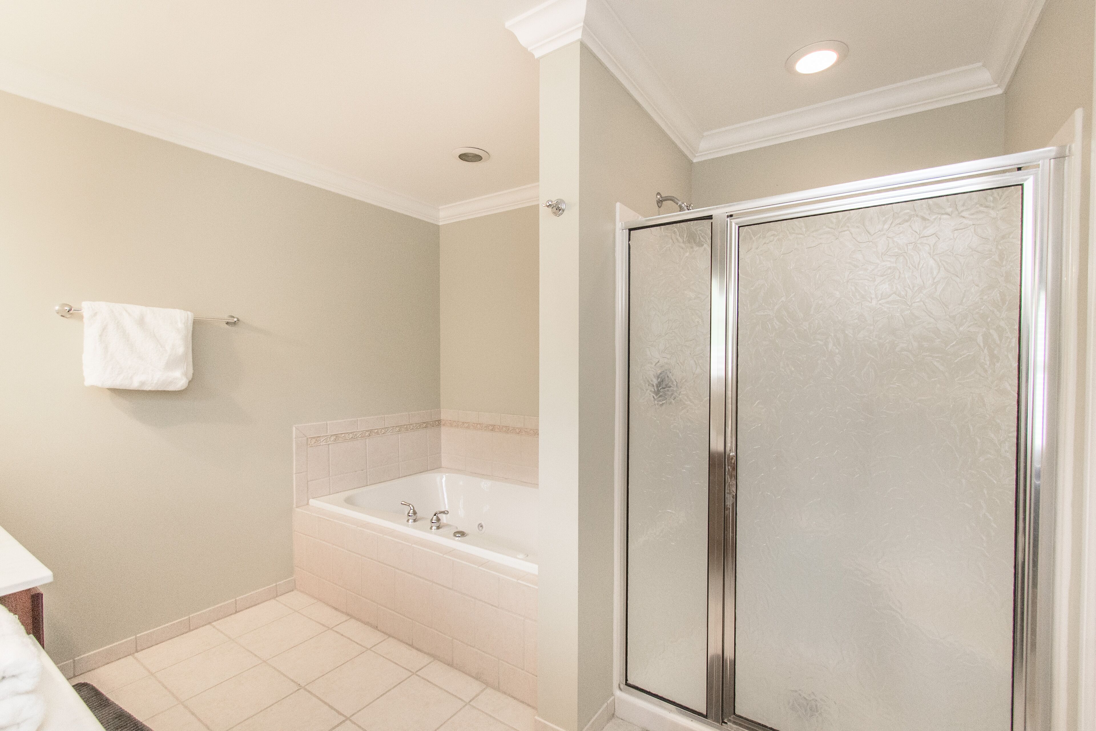 A bathroom with a bathtub, a glass shower enclosure, and a white towel hanging on the wall.