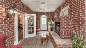 A brick-walled room with a fireplace, a ceiling fan, and a door leading to another room.